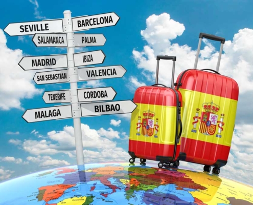 Two spanish luggages standing on the world map close to a wooden sign with many city direction