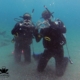 Two scuba diver doing the heart sign with the fingers while resting on their knees underwater