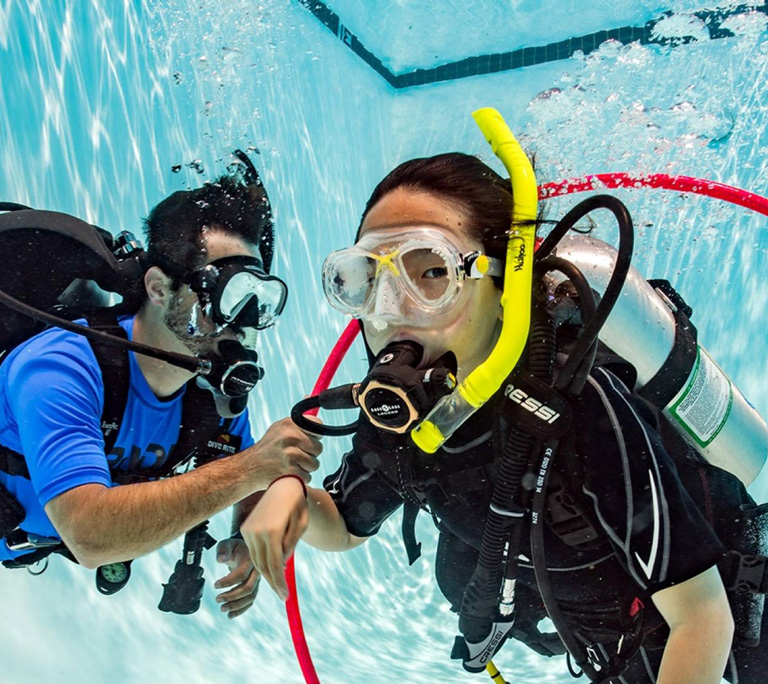 kids of 8 years old learning to scuba dive in the safe environemnt of a swimming pool with a professional diving instructor