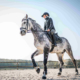 Young lady riding a write and black horse on the sand.